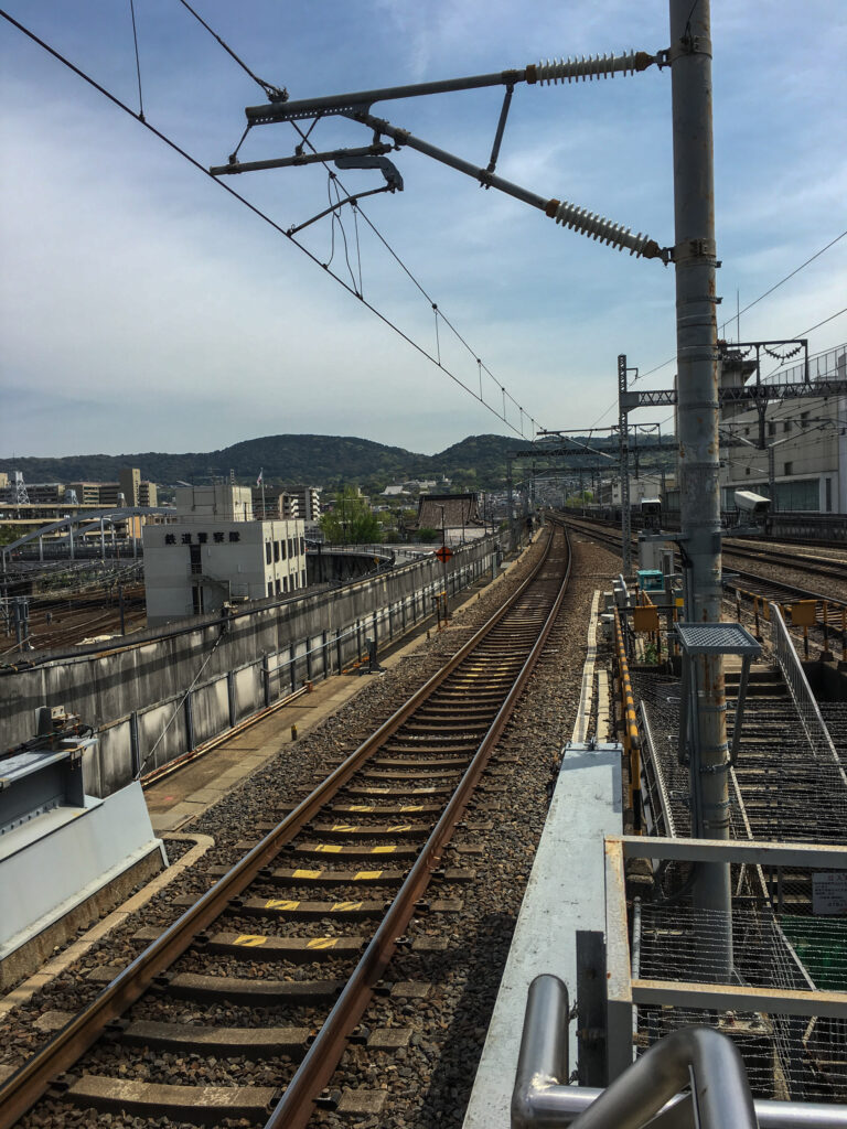 Empty rails in Japan, buildings nearby and hills in the distance.