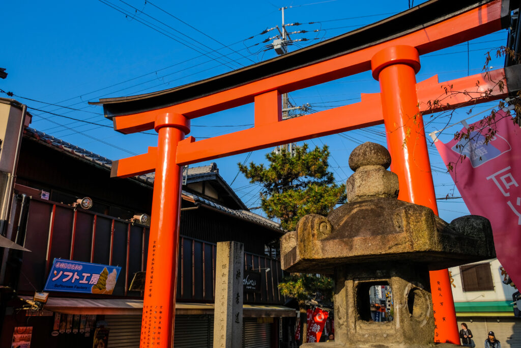 A large orange Torii in Kyoto, with a stone shrine in the foreground.