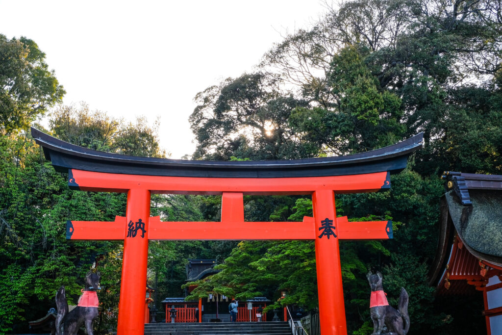 An orange and black torii, with two fox statues on either side, starting the trail up Mt. Inari.