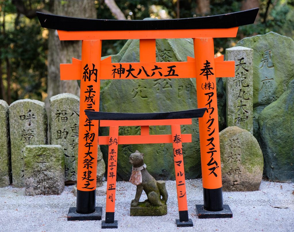 A small torii, with a smaller torii in front of it, and then a small stone fox statue beneath both.