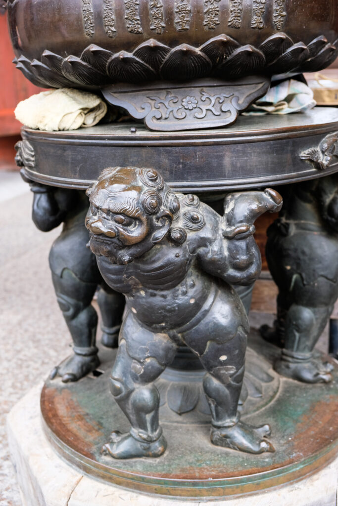 Bronze figures hold up a small table and bowl.