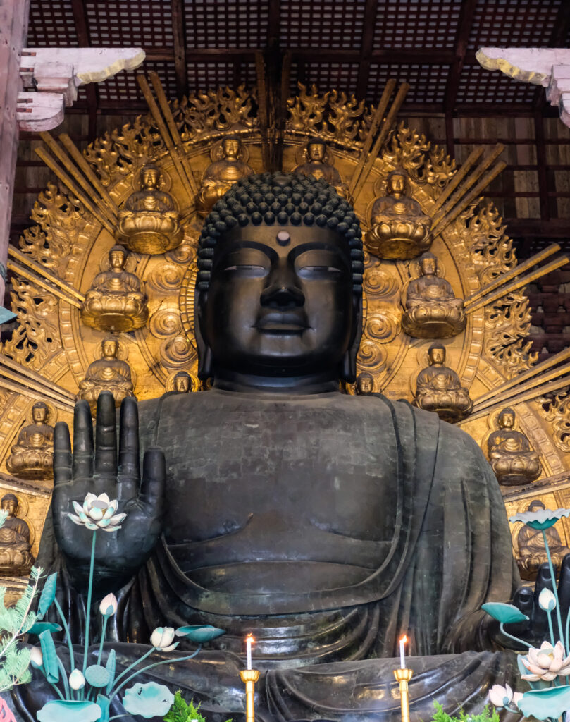 A very large black statue of the Buddha, with gold plates in the background showing smaller Buddhas.