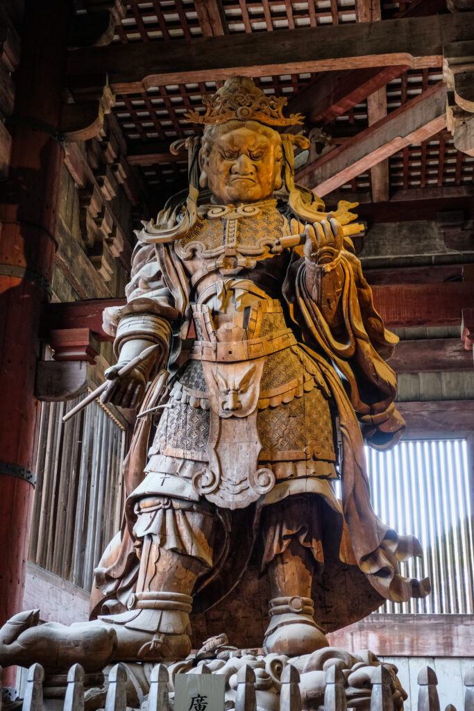 A large wooden sculpture of a figure holding a brush. The statue is roughly 20-25 feet tall.