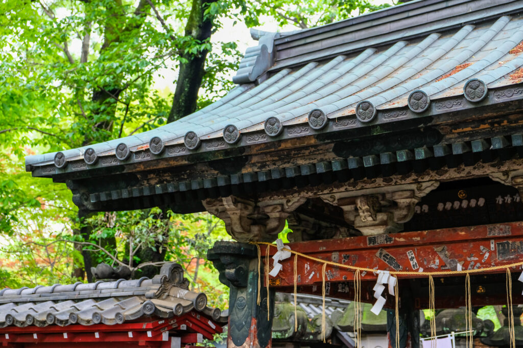 A blue-green curved roof on a shrine with a red cross-beam, in Ueno Park.