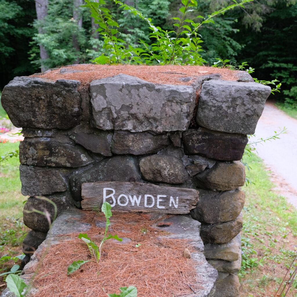 A small wooden sign saying "Bowden" propped up against a stone fence.