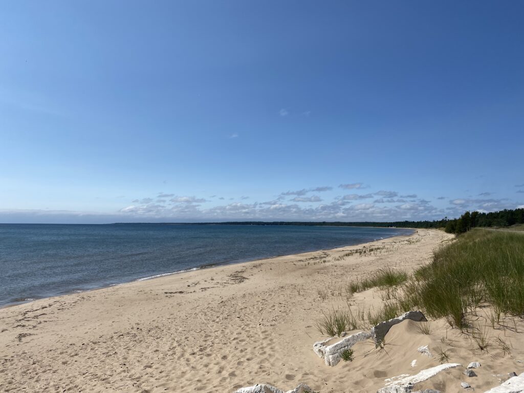 Lake Michigan from the Upper Peninsula. Blue skies, dark blue water, and a sandy beach.
