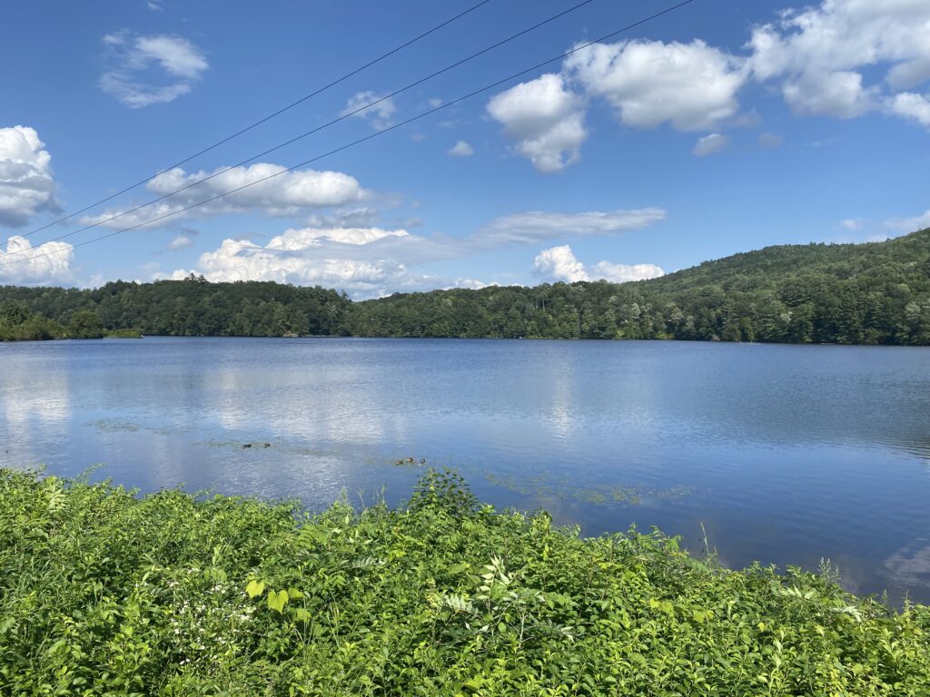 The Connecticut River in Vermont, looking east over into New Hampshire. Puffy white clouds, blue sky, reflecting on the water.