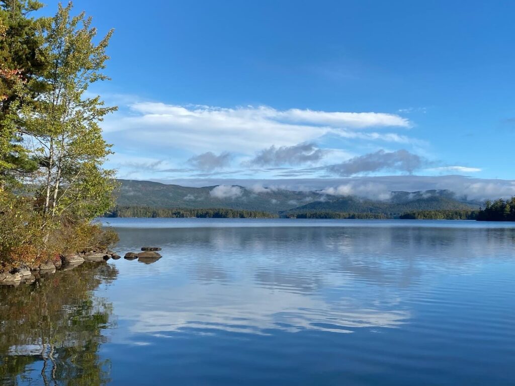 Squam Lake, looking west. Trees on the left, and in distance, some low clouds over the hills across the lake.